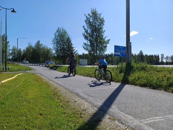 Pyöräilijöitä kevyen liikenteen väylällä, jonka vieressä kaiteen takana autoliikennettä.