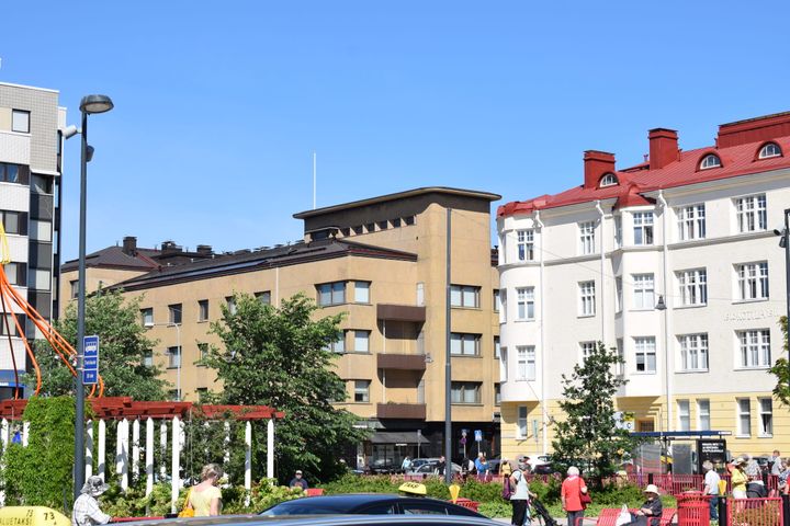 Torinäkymä Lahdesta kirkkaana päivänä, taustalla eri-ikäisiä rakennuksia ja etualalla ihmisiä liikkeellä.