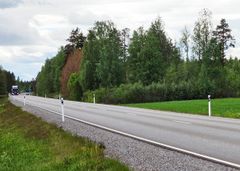 Maantie kulkee metsän vieressä pilvisenä päivänä, tien varrella näkyy liikennemerkkejä.