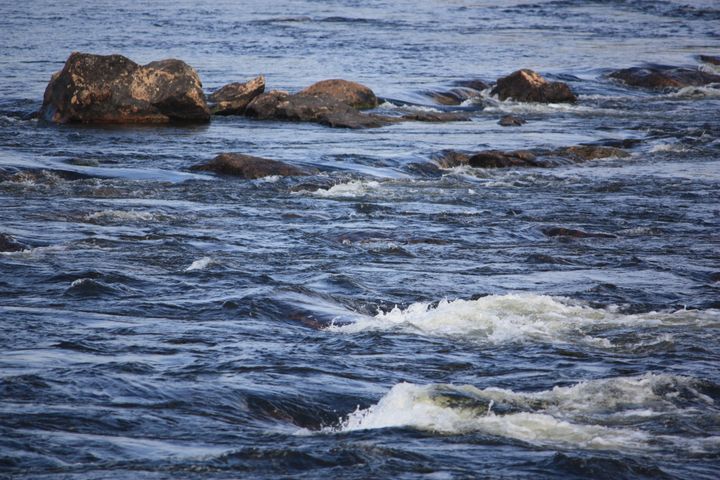 Virtaava joki, jossa näkyy kiviä veden pinnalla.