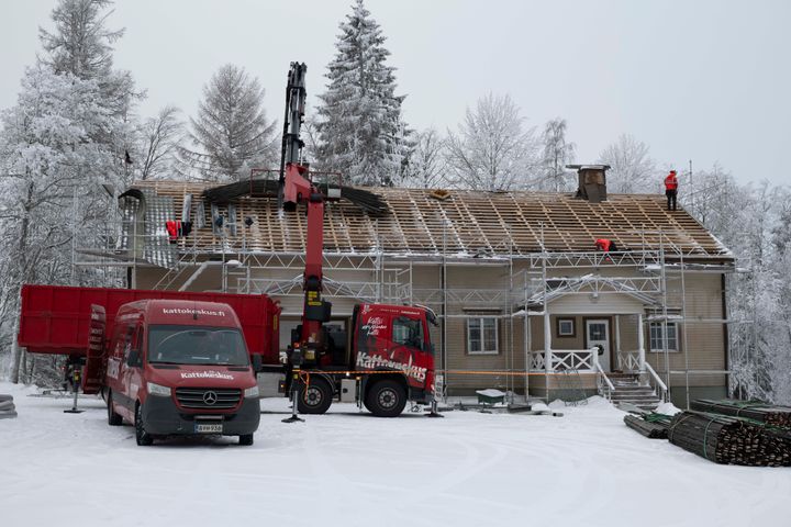 Talon kattoaa kunnostetaan, talon edessä nosturi ja pakettiauto, maassa lunta.