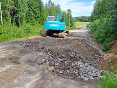 Kaivinkone työskentelee soralla peitetyn tien sortumakohdan korjaustöissä metsäisellä alueella.