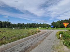 Soramainen tie, jonka ympärillä on vihreää metsää ja peltoa, sekä liikennemerkki.
