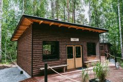 Koivujen katveessa sijaitseva tummasta laudasta tehty ulkorakennus, jossa puinen terassi
