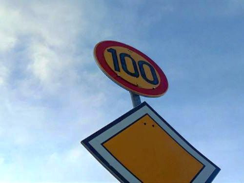 Sata kilometriä tunnissa nopeusrajoituskyltti, taustalla taivasta.