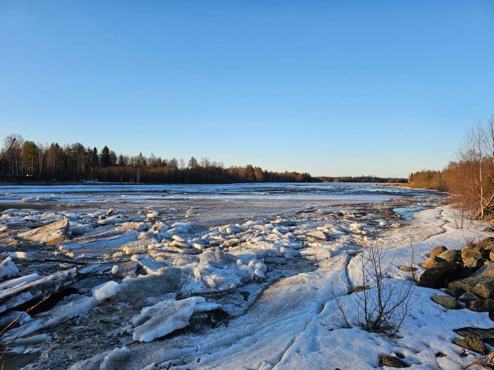 Joki, jossa rannoilla jäätä ja kauempana sulaa, kirkas sää.