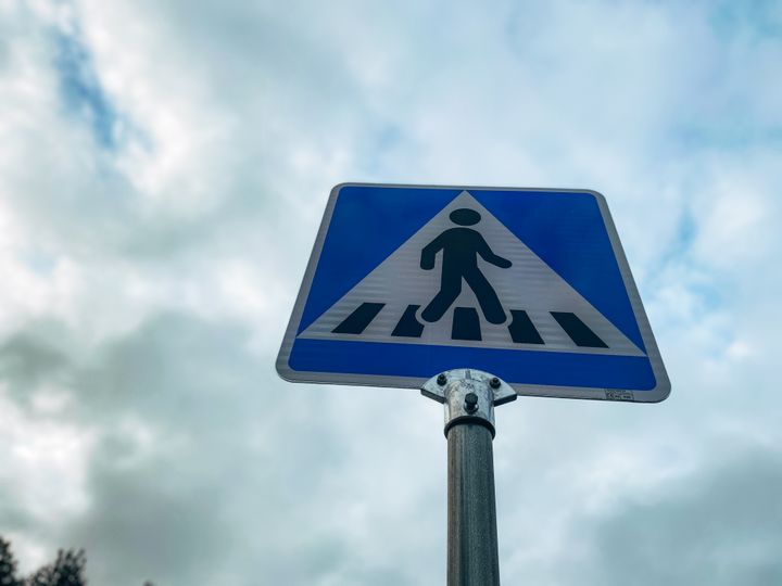 Suojatiemerkki alhaaltapäin kuvattuna, taustalla pilvistä taivasta.
