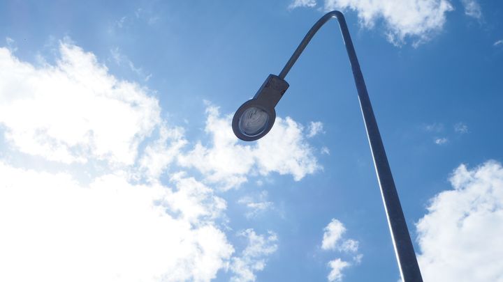 Valaisinpylväs alhaaltapäin kuvattuna, taustalla sinistä taivasta, jossa pilviä.