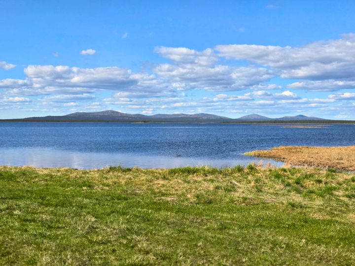 Järven ranta, tyyni järvi, taustalla tunturimaisemaa.
