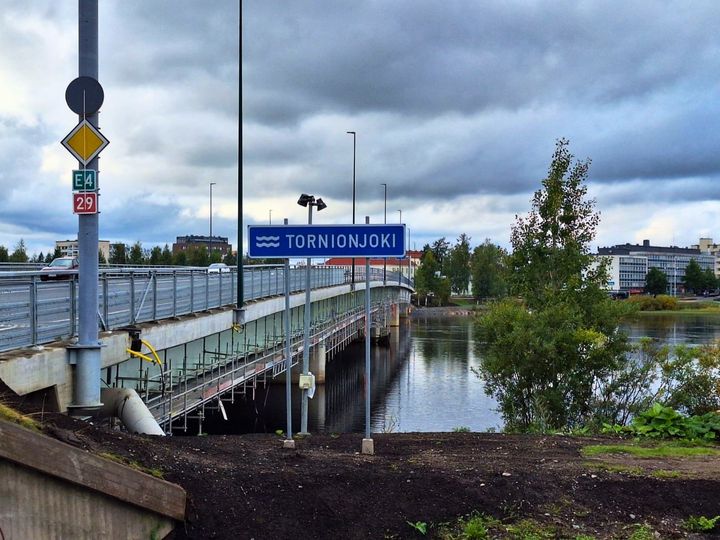 Tornionjoen silta rannalta kuvattuan, Tornionjoki-kyltti, taustalla Tornion kaupunki.
