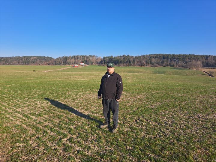 Mies tummissa vaatteissa seisoo pellolla.