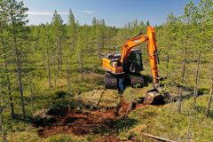 Kaivinkone työskentelee metsäisessä suomaisemassa.