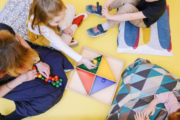 Lattialla lapsia leikkimässä aikuisen kanssa.