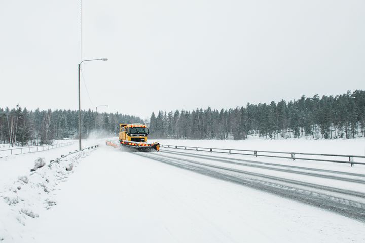 Aura-auto poistaa lunta talviselta maantieltä lumisessa metsänmaisemassa.
