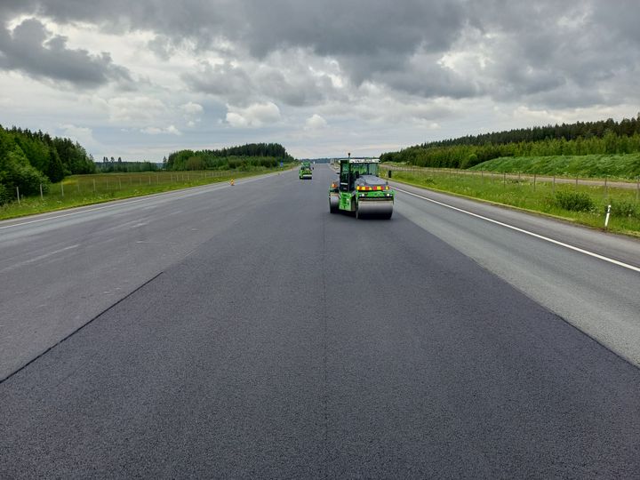 En beläggningsmaskin lägger ny asfalt på en flerfilig väg i landsbygdsmiljö.