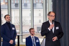 Kolme miestä seisoo ja puhuu sisätiloissa ikkunan edessä.