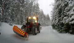 Aura-auto auraa lumen peittämää metsätietä talvimaisemassa.