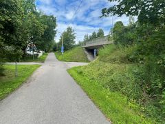 Jalankulun ja pyöräilyn väylä risteyksessä alikulun läheisyydessä. Oikealla näkyy sillan alikulku, liikennemerkkejä sekä nurmikkoa ja puustoa väylän ympärillä.