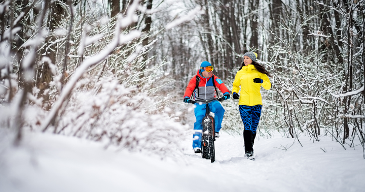 En person cyklar och en annan joggar bredvid på en snöig skogsstig.
