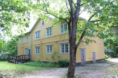 Kaksikerroksinen keltainen puutalo vehreässä ympäristössä.