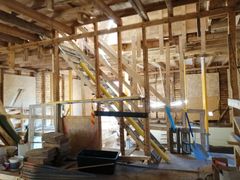 Kuvan rakennuksessa on näkyvissä puurakenteita, tuentoja, keskeneräinen purku- ja kunnostustyö, ikkunoita ja rakennusmateriaaleja.