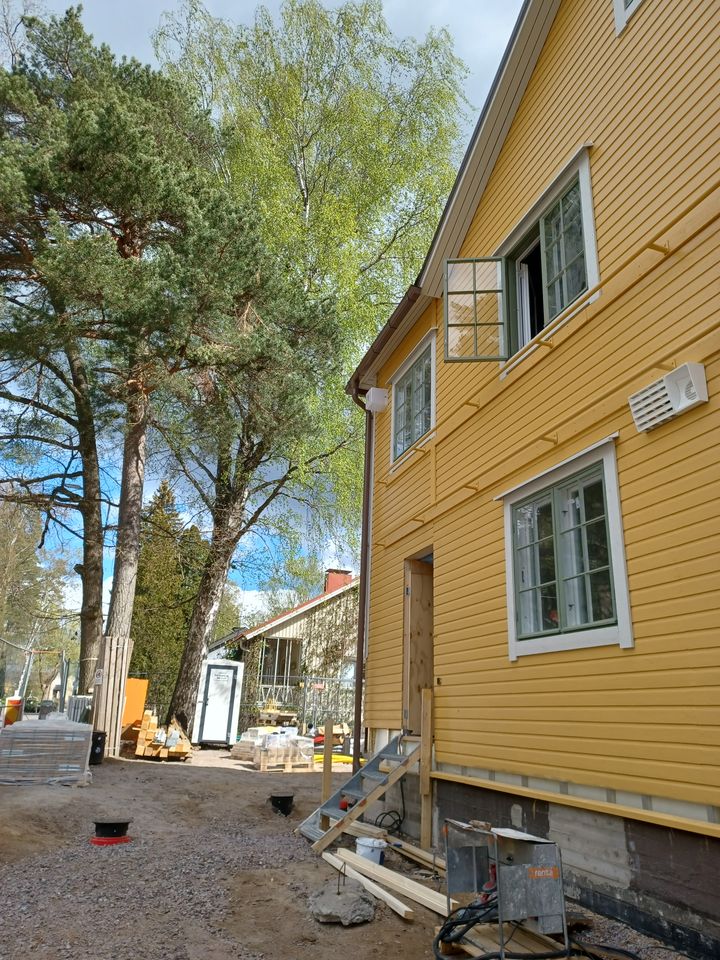 Keltainen puutalo, jossa on vastamaalatut ikkunat ja seinät. Ympäristössä näkyy korjausrakentamisen merkkejä, kuten rakennustarvikkeita ja telineitä.