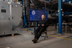 Henkilö istuu tuolilla teollisessa ympäristössä ja pitää tablettia kädessään, taustalla suuri näyttö.