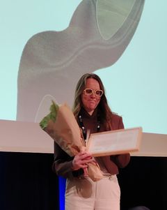 Tuulia Nikula vastaanottaa kukat ja tunnustuspalkinnon seminaarin lavalla.