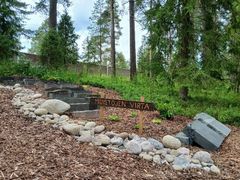Kivillä reunustettu polku ja "Muistojen virta" -kyltti metsäisellä hautausmaan muistolehtoalueella.