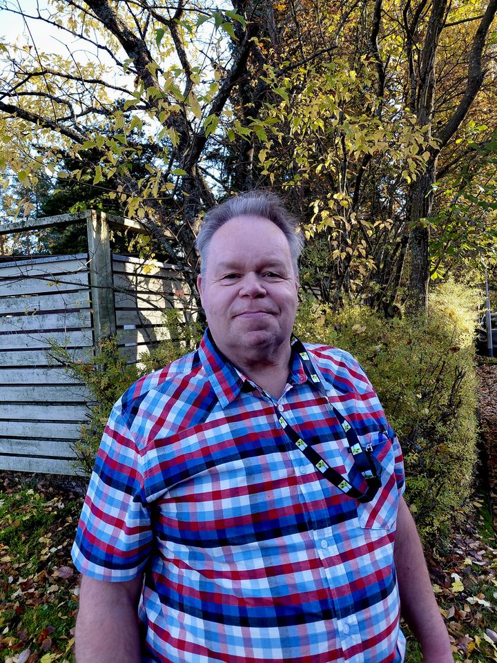 Ruutupaitainen mies seisoo syksyisellä pihalla.