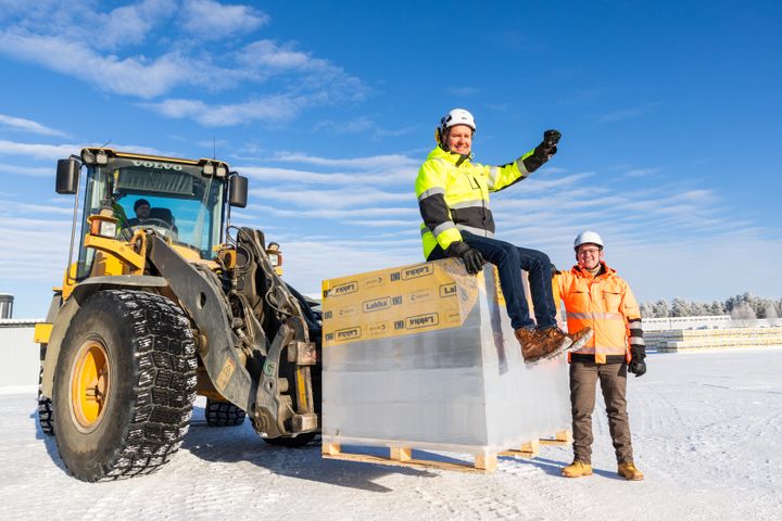 Kuvassa kaksi miestä työpukineissa. Toinen istuu kuorman päällä ja toinen seisoo. Miehet hymyilevät tyytyväisinä.