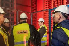 Pieni ryhmä ihmisiä keltaisissa huomioliiveissä ja kypärissä, seisomassa teollisuusympäristössä.