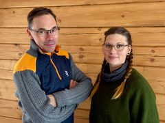 Kaksi henkilöä, Risto Haikonen ja Anna-Leena Haikonen seisovat hirsiseinän edessä.