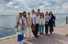 Yhdeksän nuorta aikuista ryhmäkuvassa, taustalla näkyy meri.