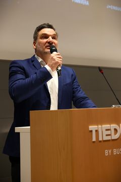 Mies sinisessä puvussa puhuu mikkiin puhujakopissa.