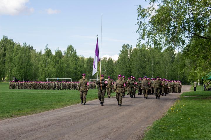 Maastopukuisia naisia marssii pois kentältä, etualalla kannetaan Naisten Valmiusliiton lippua.