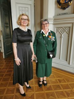 Kaksi naista seisoo pukeutuneina juhla-asuihin sisätilassa Naisten Valmiusliiton 25-vuotisjuhlassa Ritarihuoneella vuonna 2022.