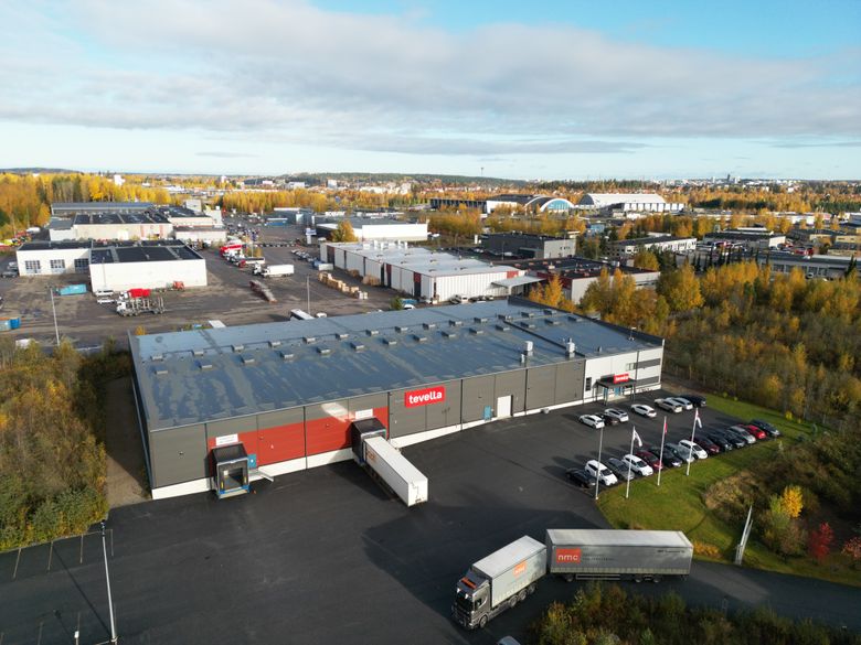 Ilmakuva Tevellan toimitiloista Tampereen Sarankulmassa. Rakennuksen edessä on pysäköityjä autoja ja lastausalueella rekkoja.