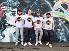 Neljä Terassimölkky ry:n perustajajäsentä poseeraa värikkään graffitiseinän edessä pelipaidoissaan.