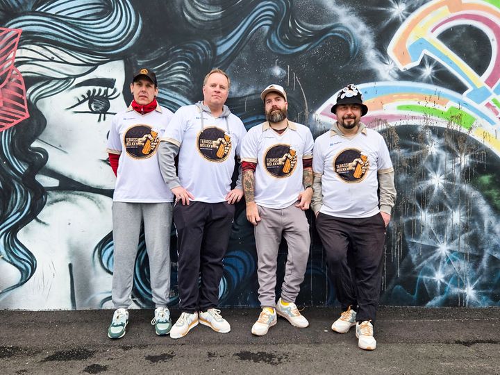 Neljä Terassimölkky ry:n perustajajäsentä poseeraa värikkään graffitiseinän edessä pelipaidoissaan.