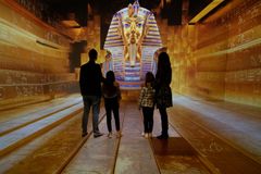 Neljä ihmistä seisoo valaistussa huoneessa, jonka seinillä on egyptiläisiä hieroglyfejä ja suuri faaraon naamio.