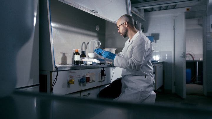 Tutkija työskentelee valkoisessa takissa laboratoriossa.