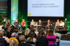 Apuvälinetapahtuman ohjelmalavalla menossa paneelikeskustelu. Kuva otettu yleisön takaa, joten kuvan etualalla näkyy yleisöä ja kuvan takana lava, missä paneelikeskuslijat.