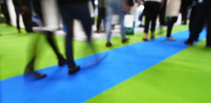 Ihmisiä kävelemässä tapahtumassa, jossa on vihreitä ja sinisiä mattoja.