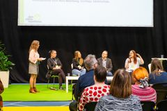 Nina Malmberg seisoo vasemmassa reunassa, panelistit istuvat vieretysten, yleisöä näkyy etualalla.