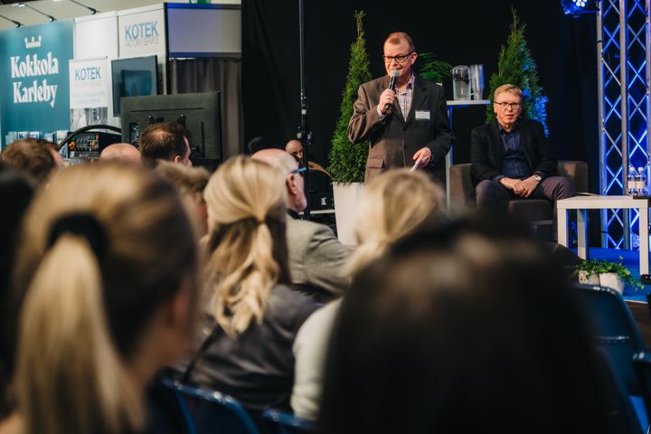 Lavalla Esa Pellikainen ja Oulun kauppakamarin Suurhankeinfo, edustalla yleisöä kuuntelemassa