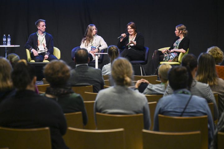 Paneelikeskustelu, jossa neljä henkilöä istuu puhujatuoleilla yleisön edessä Helsingin Messukeskuksessa.